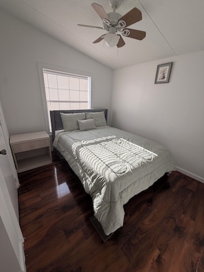 A bedroom with a bed, a nightstand, a ceiling fan, a window with blinds, and a framed picture on the wall. - Charming 3-bedroom house with AC in Elkridge awaits you (Elkridge)
