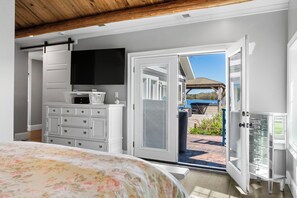 A bedroom with a bed, dresser, television, and a sliding glass door leading to an outdoor patio.