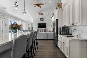 A modern kitchen with white cabinetry, a central island with bar stools, a large refrigerator, and a flat-screen TV.