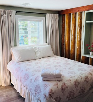 A bedroom with a bed, curtains, a window with blinds, and a wooden wall.