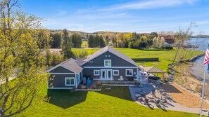 A two-story house with a large deck, a fire pit, and a view of a lake.
