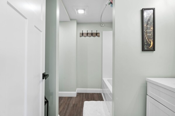 A hallway with a white door, a white wall, a ceiling light, a towel on the floor, and a framed picture on the wall.