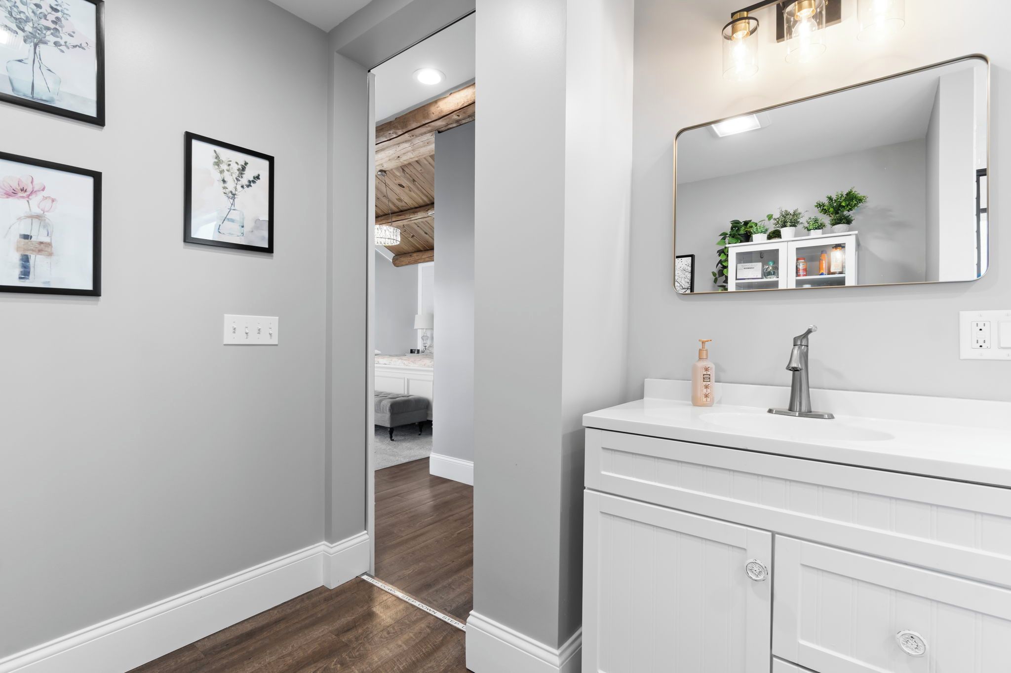 A modern bathroom with a white vanity, a large mirror, and framed artwork on the wall.