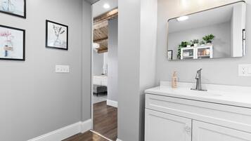 A modern bathroom with a white vanity, a large mirror, and framed artwork on the wall.