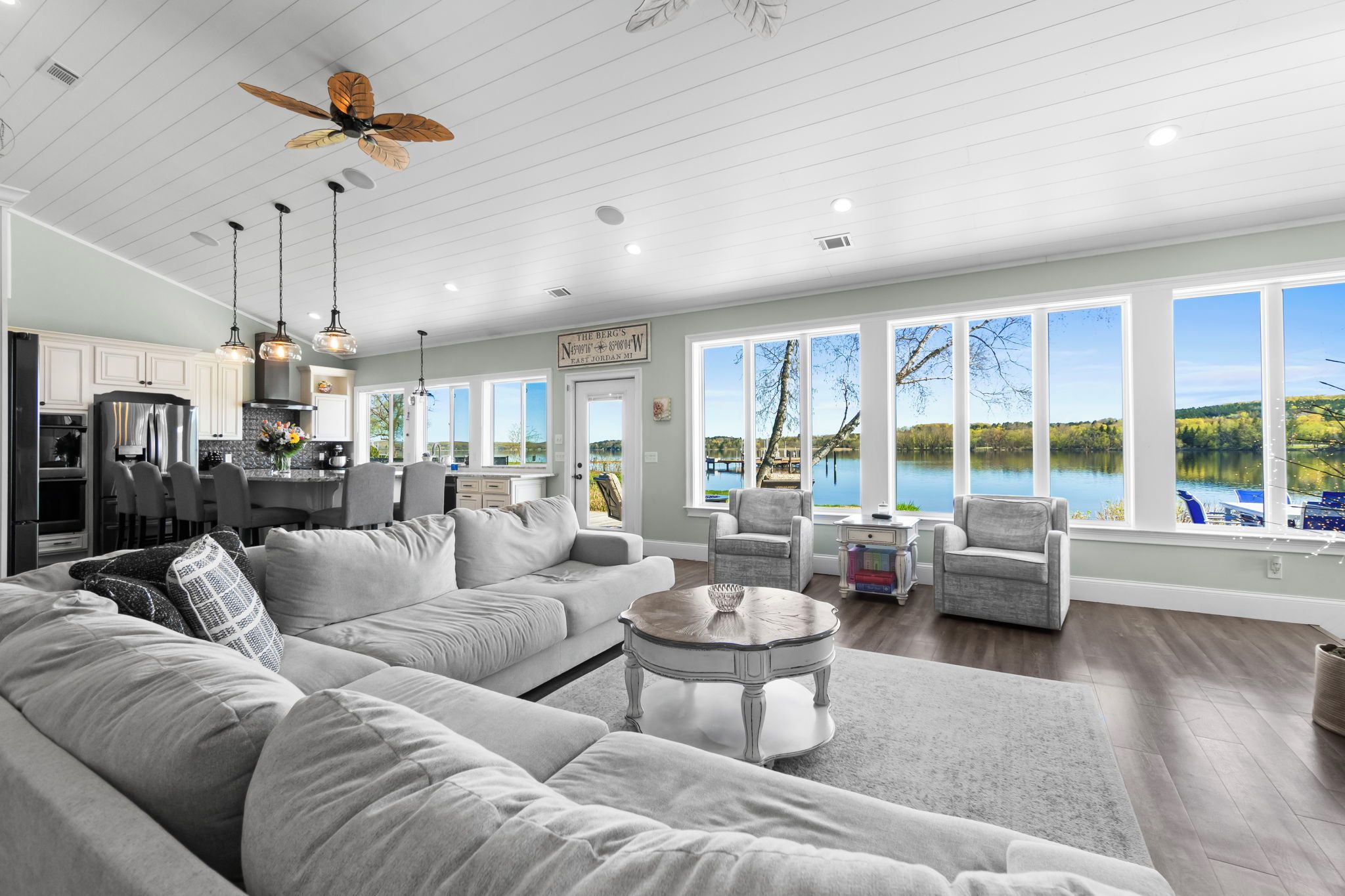 A spacious living room with a large sectional sofa, a coffee table, and a view of a lake through large windows.