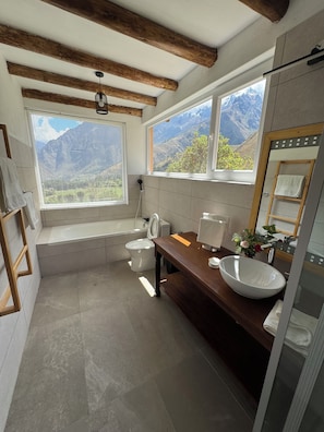 Un baño con bañera, inodoro y lavamanos, que cuenta con un ventanal con vistas a la montaña.