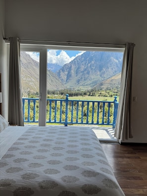 Une chambre avec un grand lit, une vue sur les montagnes par une porte ouverte et une balustrade bleue.