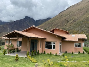 A two-story house with a tiled roof, a porch, and a well-maintained lawn with small trees and flowers. - Fantastic 4-bedroom house in Cusco perfect for your getaway (Cusco)