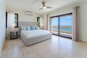 A bedroom with a bed, a nightstand, a ceiling fan, and a view of the sea through a balcony. - Sunkiss Villa in Cole Bay with breathtaking views (Koolbaai)