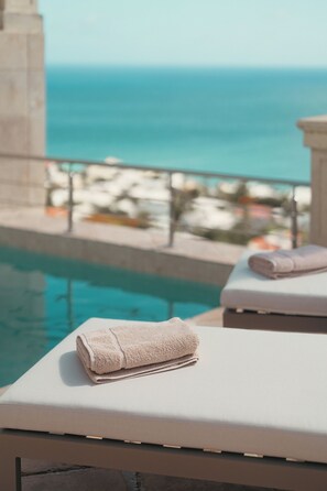 A poolside area with lounge chairs and a towel, overlooking a pool and a beach with umbrellas. - Sunkiss Villa in Cole Bay with breathtaking views (Koolbaai)