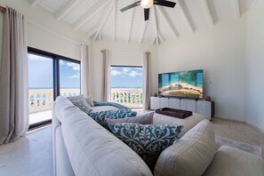 A spacious living room with a large window, a ceiling fan, and a flat-screen TV. - Sunkiss Villa in Cole Bay with breathtaking views (Koolbaai)