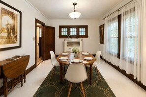 A dining room with a round table set for six, flanked by white chairs, a green patterned rug, and a wooden cabinet. - Peabody Park Retreat | Sleeps 5 | Fire Pit (Appleton)