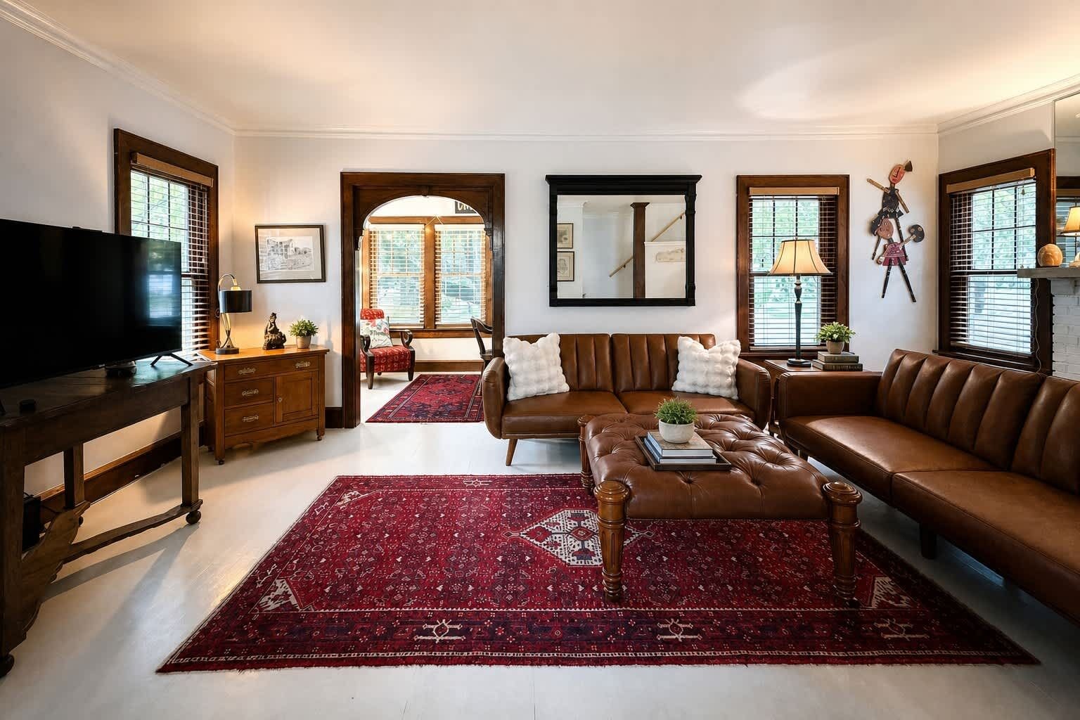 A living room with a brown leather sofa, a red patterned rug, a television on a wooden stand, and a wooden cabinet.