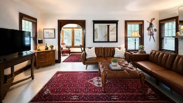 A living room with a brown leather sofa, a red patterned rug, a television on a wooden stand, and a wooden cabinet.