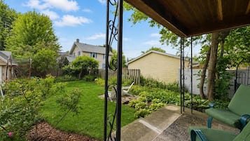 A covered patio area with a green chair, a swing set, and a garden with various plants and a lawn.