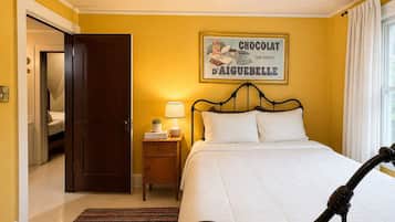 Een hotelkamer met een bed, nachtkastje met lamp, een lijst met afbeelding aan de muur, en een raam met gordijnen.
