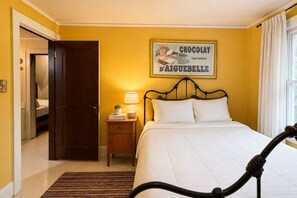 A hotel room with a bed, a nightstand with a lamp, a framed picture on the wall, and a window with curtains. - Peabody Park Retreat | Sleeps 5 | Fire Pit (Appleton)
