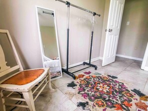 Ein Zimmer mit einem Sessel, einem Spiegel, einem Standventilator und einem gemusterten Teppich.