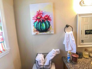 A bathroom with a painting of flowers, a towel rack, and a sink with toiletries. - Cozy 2-bedroom house in adorable Arabi with AC (Arabi)