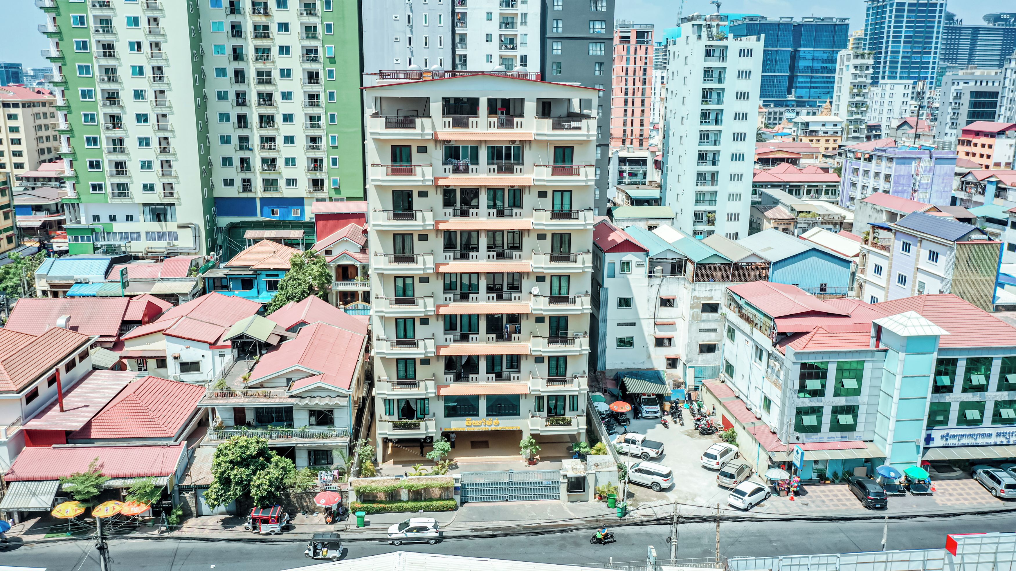 A multi-story building with balconies, a parking lot, and a street with vehicles.