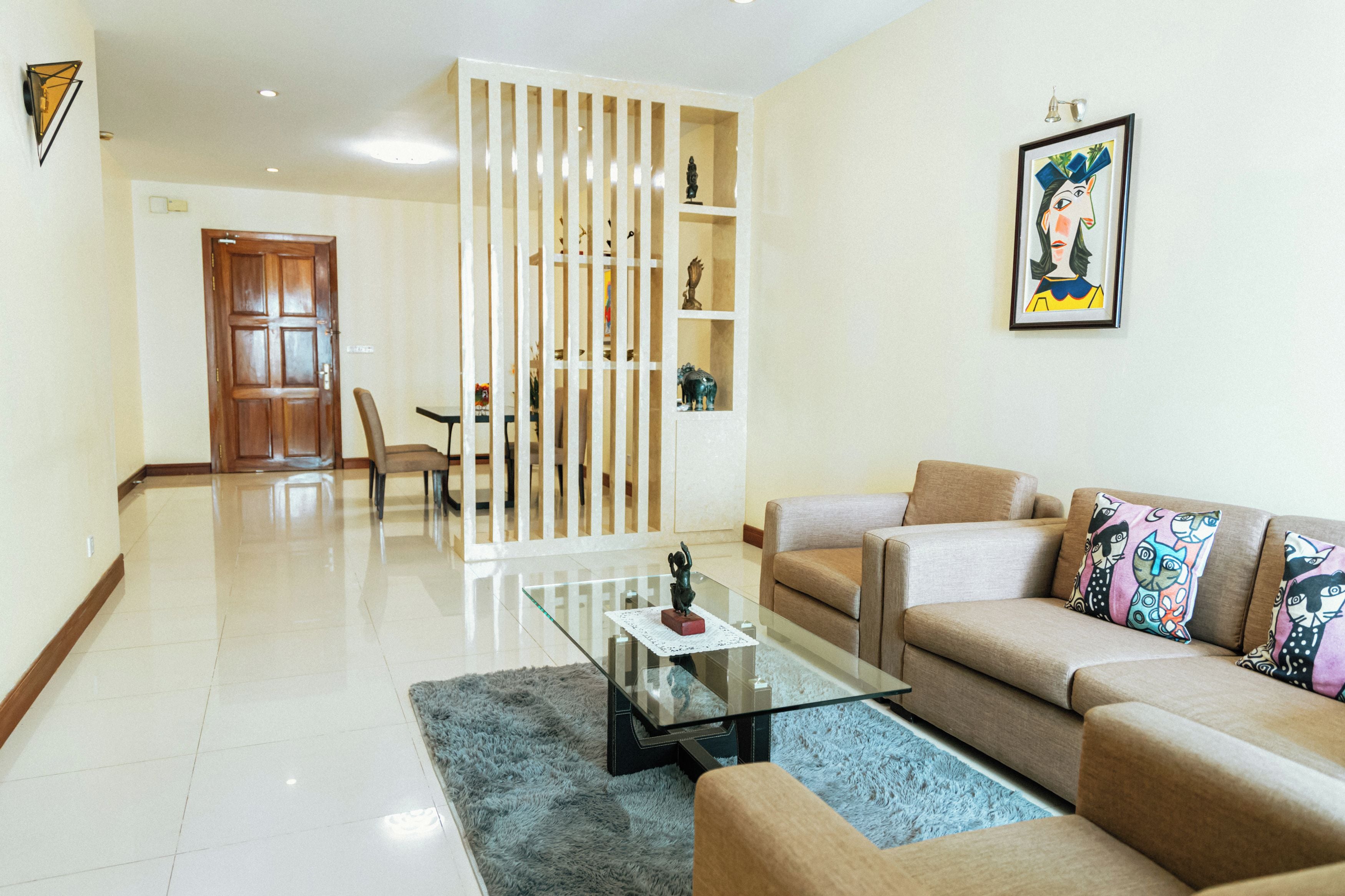 A living room with a glass coffee table, beige sofa, and colorful cushions.