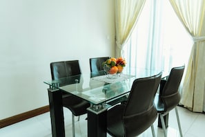 Un comedor moderno con una mesa de vidrio, cuatro sillas negras y un frutero sobre la mesa.