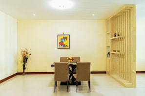 Un área de comedor con una mesa y sillas, un jarrón con flores, una obra de arte enmarcada en la pared y una estantería de madera.