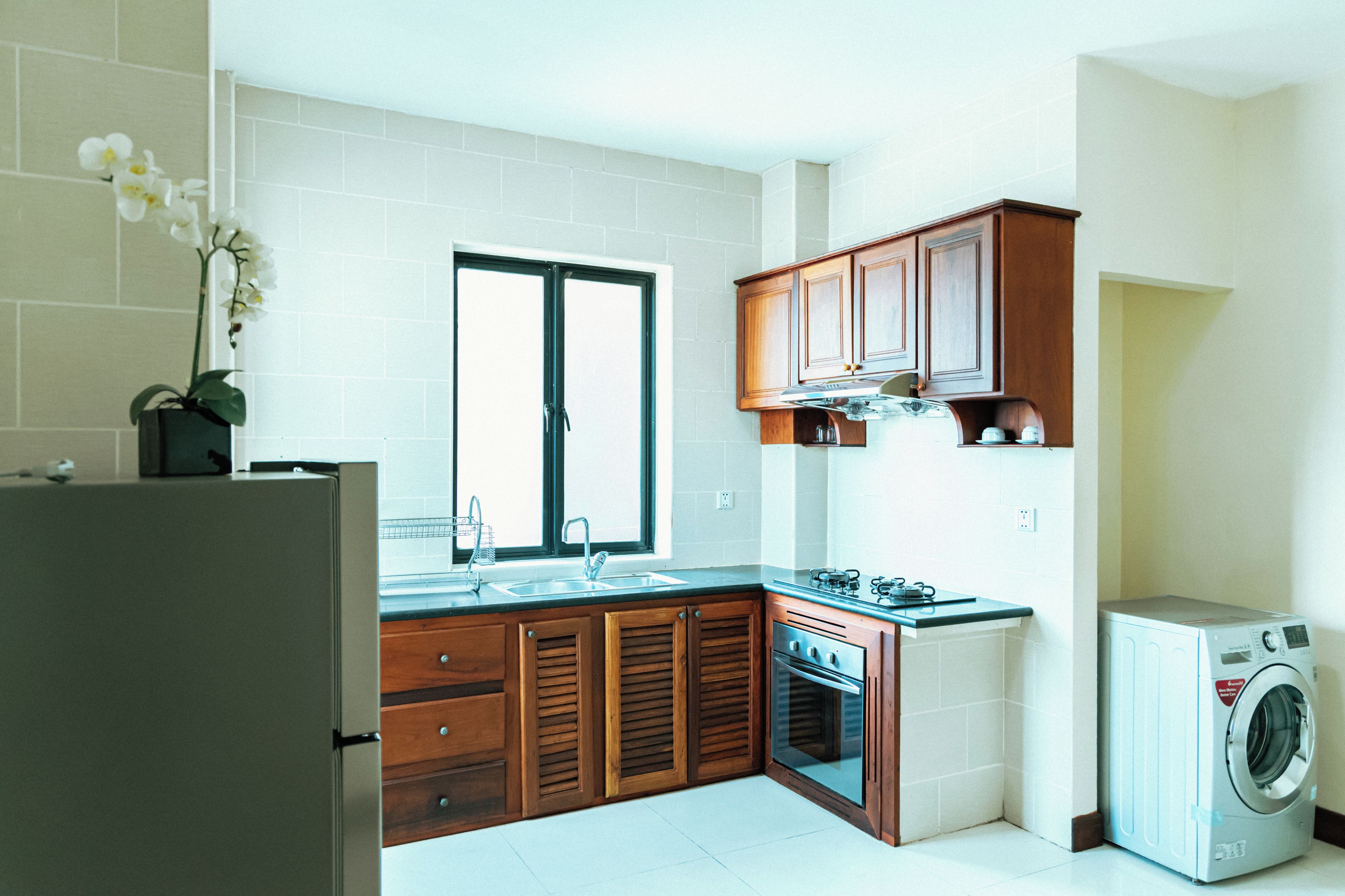 A modern kitchen with wooden cabinets, a built-in oven, a sink, and a washing machine.