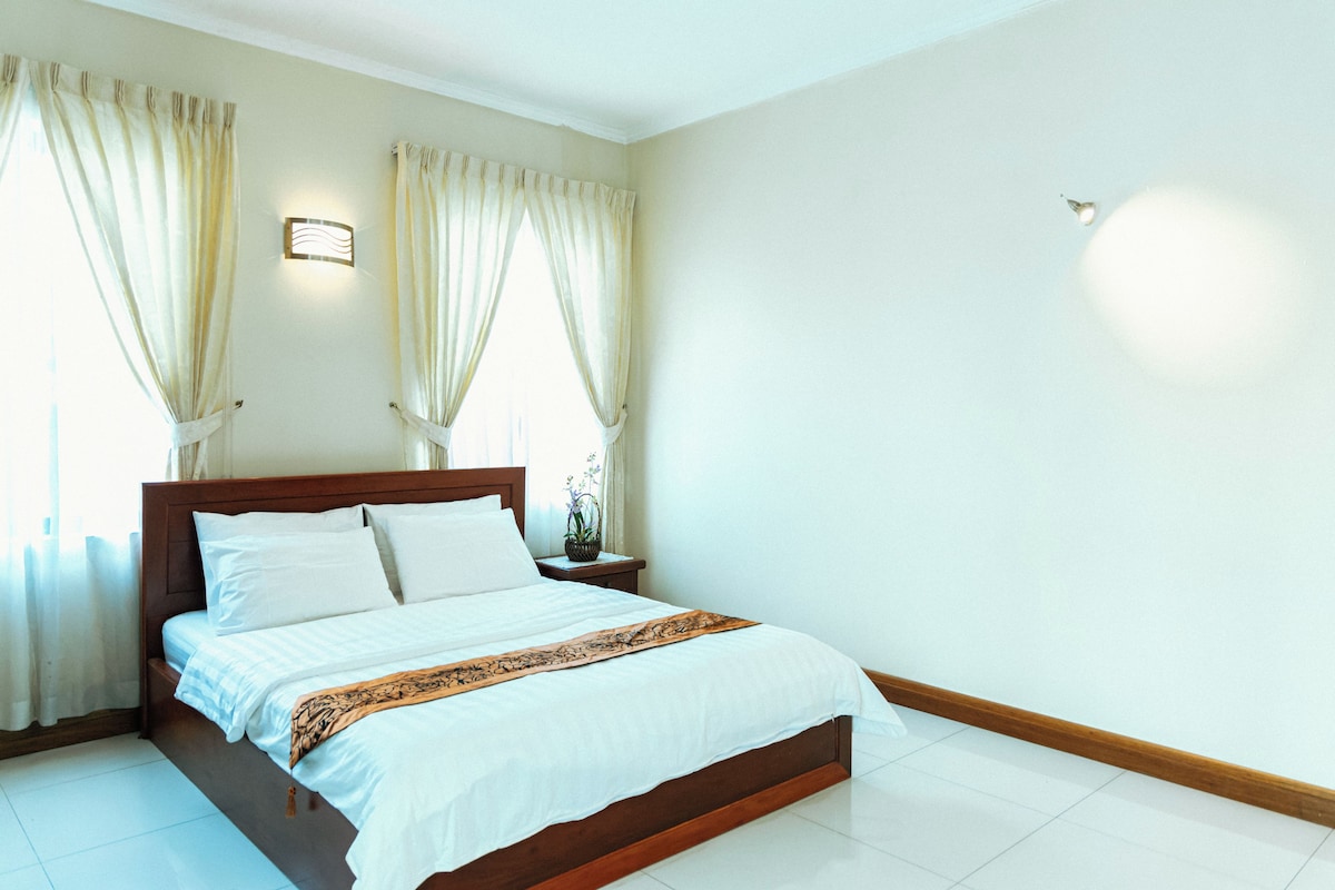 Quarto de hotel com cama de madeira, roupa de cama branca e cortinas.
