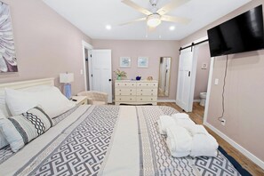 Une chambre à coucher comprenant un lit, une table de chevet, une lampe, une commode et un ventilateur de plafond.