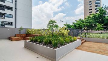 A rooftop garden with planters, wooden steps, and a metal railing.
