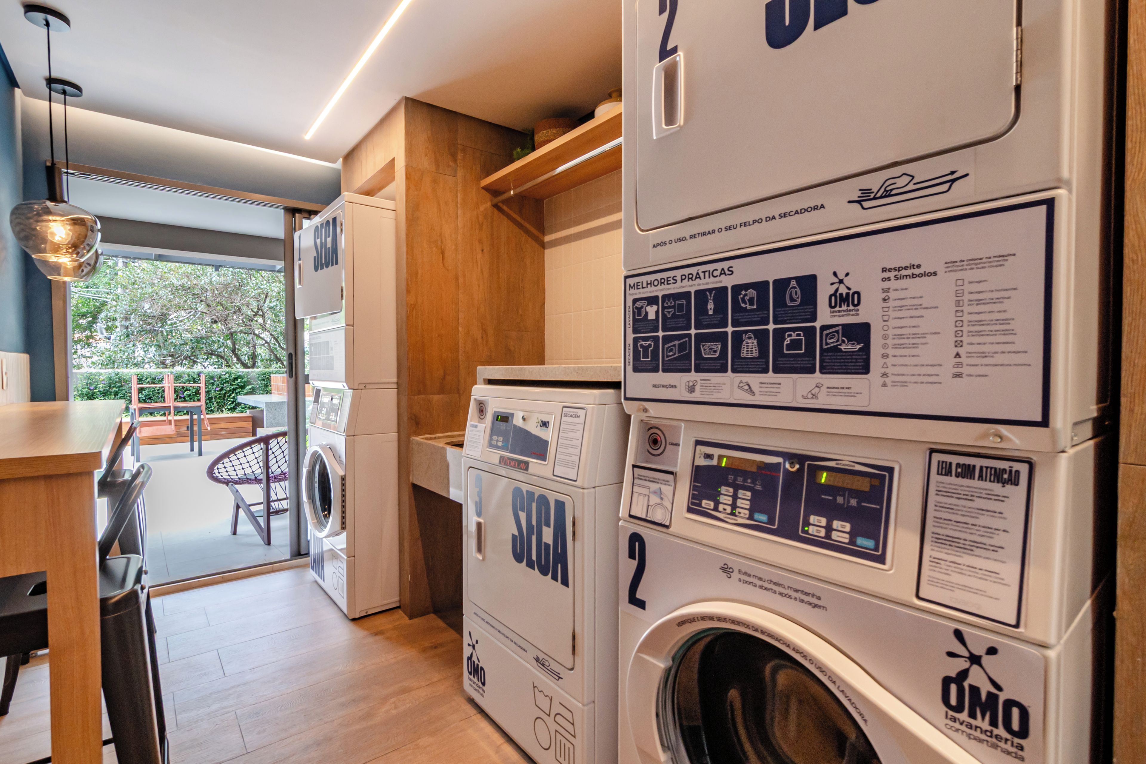 A laundry area with stacked washing machines, a wooden bench, and a view of the outdoors.