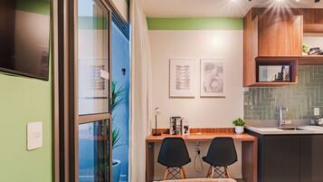A modern kitchen with a built-in stove, a sink, and a wooden cabinet above the counter. There is a dining area with two chairs and a table, and a bed with a white headboard.
