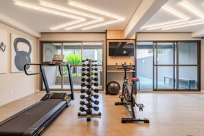 Un gimnasio moderno en casa con cinta de correr, soporte para pesas, bicicleta estática y pelota de ejercicio.