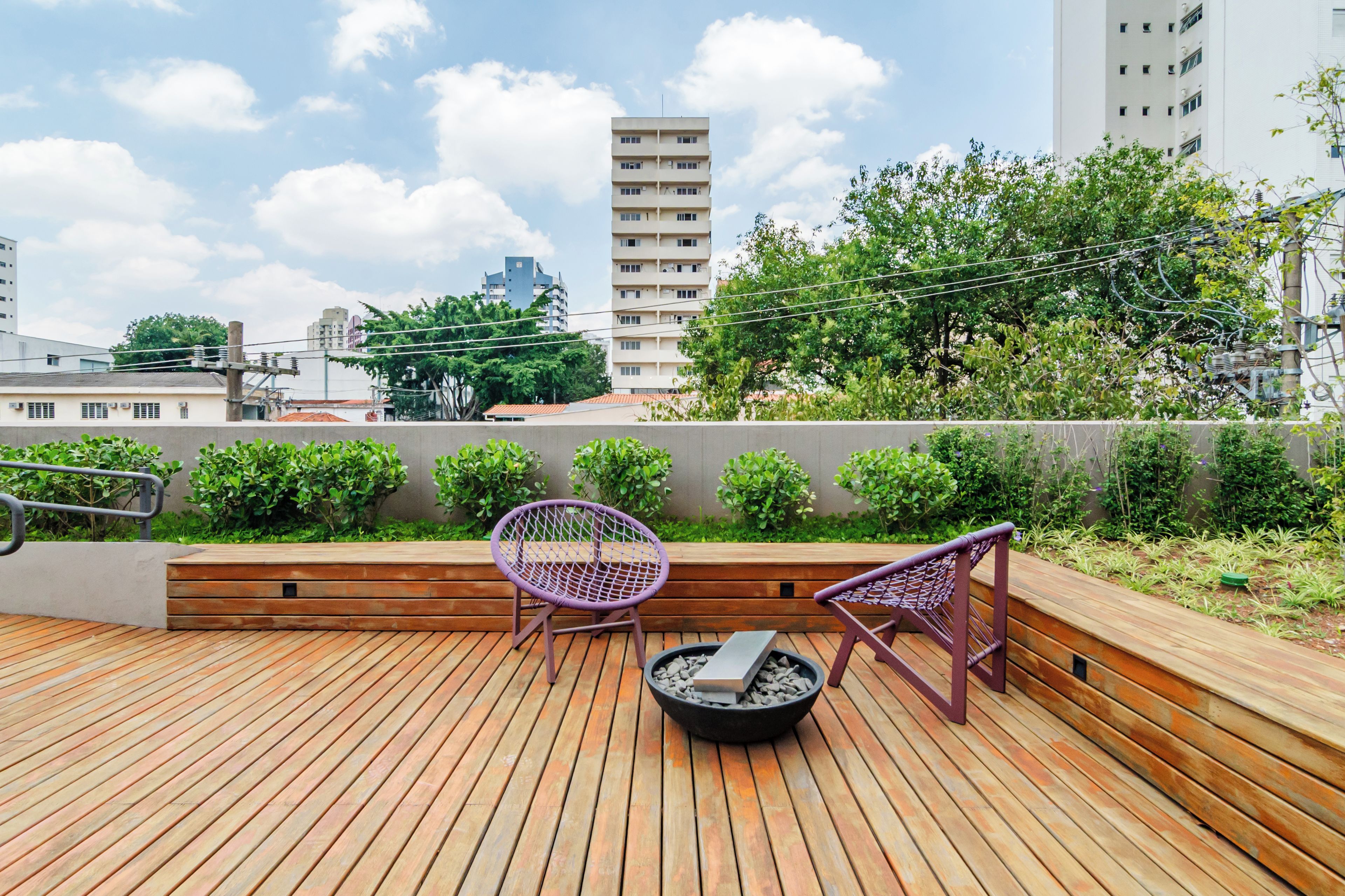 Um terraço no telhado com piso de madeira, duas cadeiras roxas e uma pequena lareira.