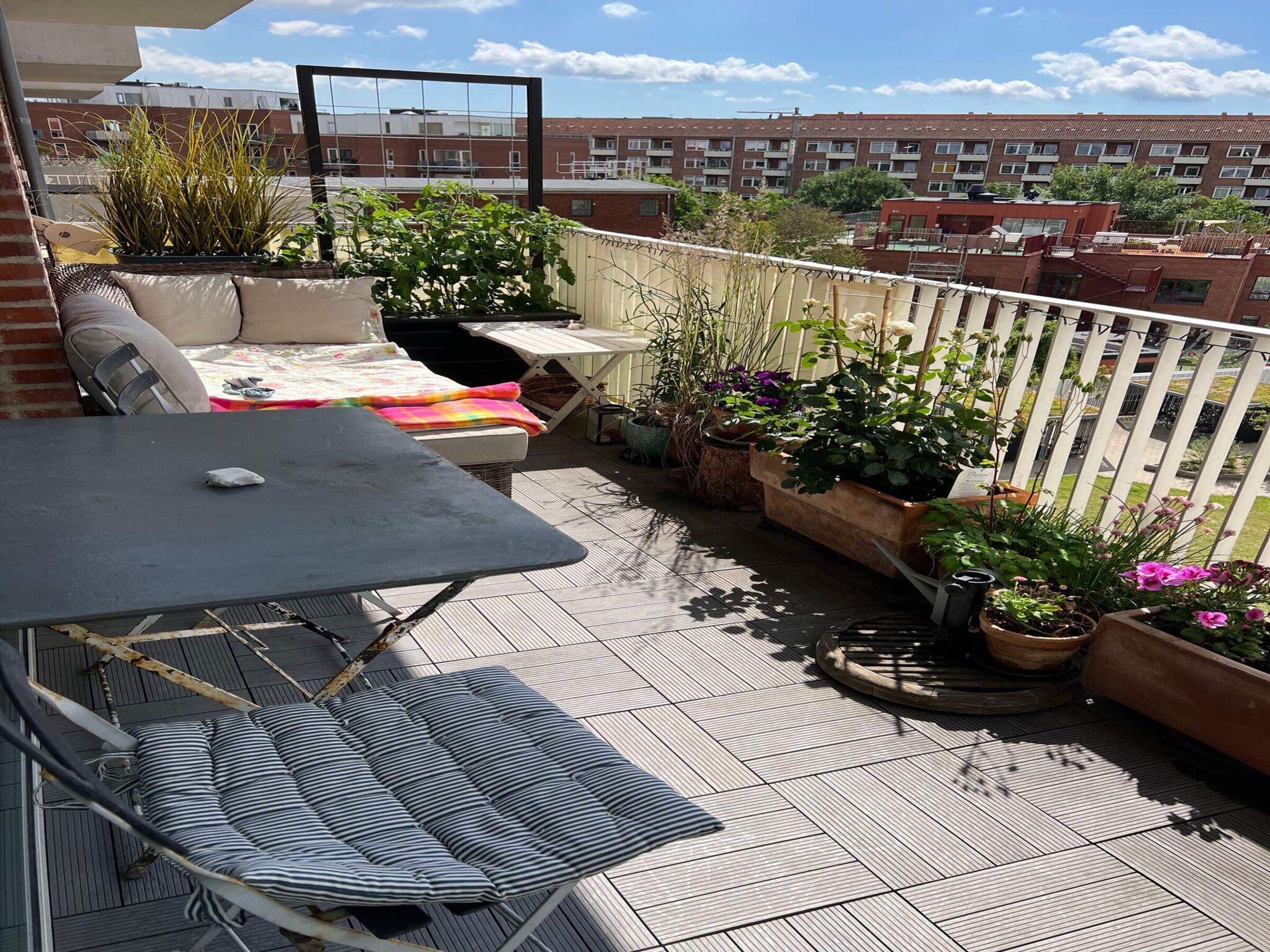 A rooftop terrace with a table, chairs, and potted plants.