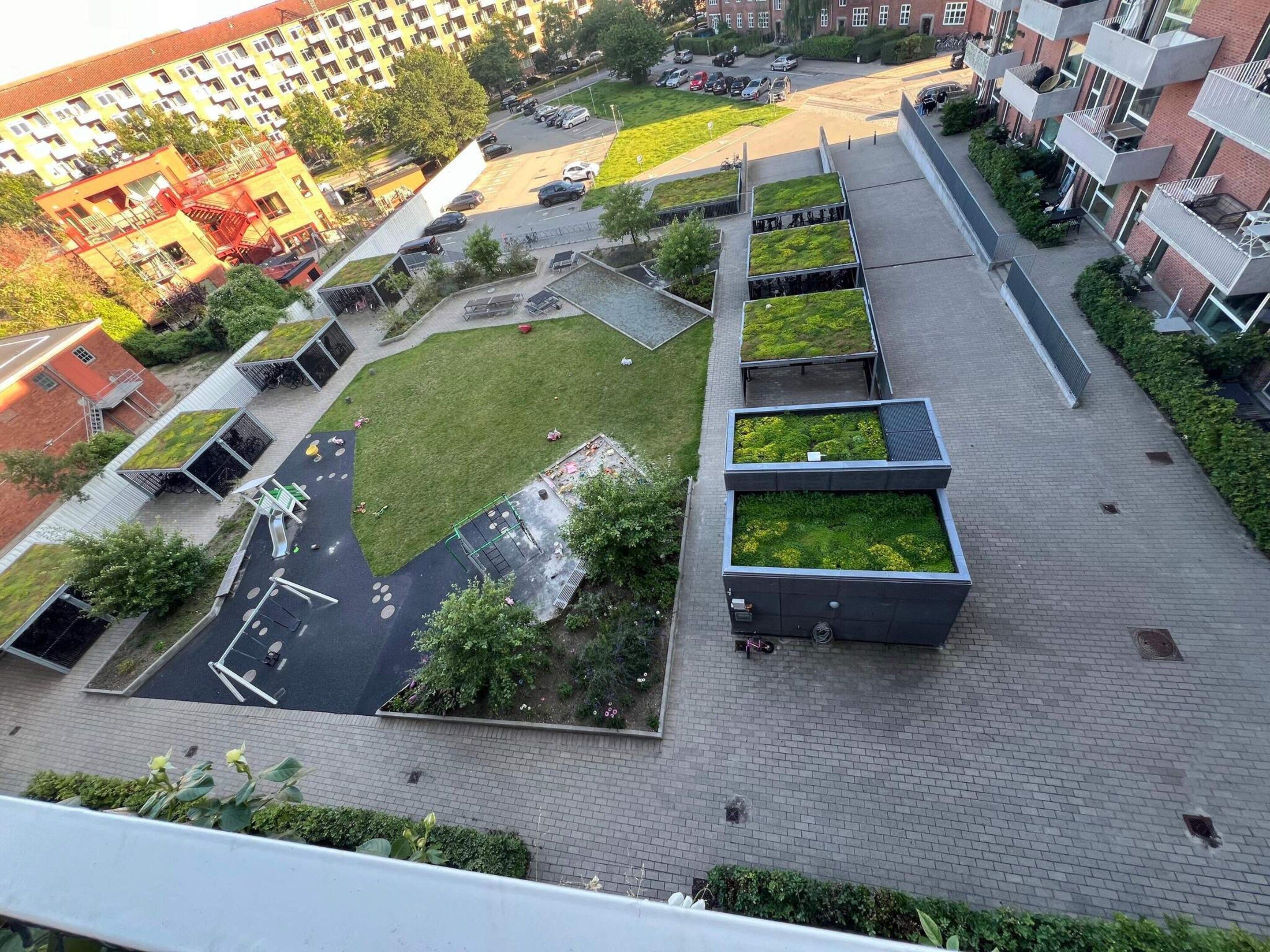 An aerial view of a residential area with multiple buildings, green roofs, and a parking lot.