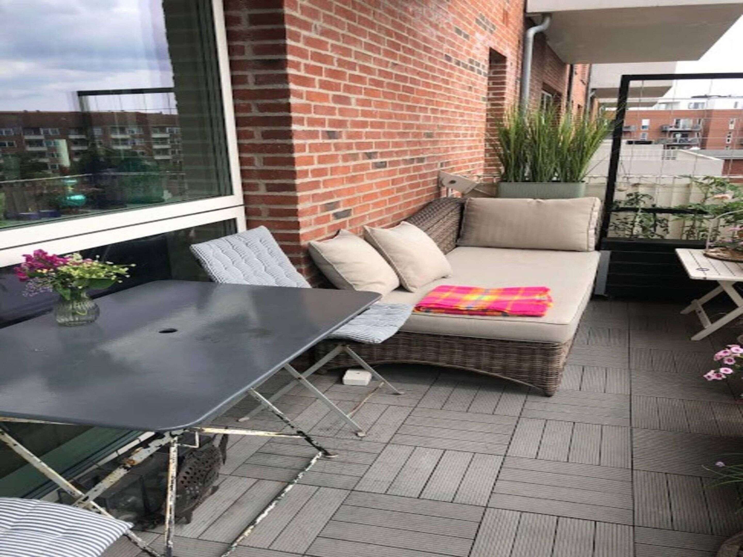 A balcony with a wicker sofa, a table, and a potted plant.