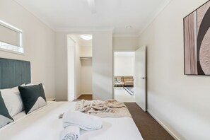 Een hotelkamer met een bed, een nachtkastje, een raam en een deur die naar een andere kamer leidt.