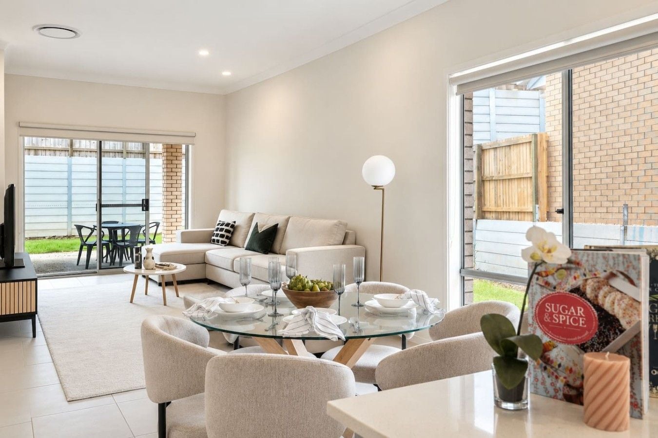 A modern living room with a glass dining table, sofas, and a television.