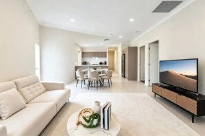 Een moderne woonkamer met een bank, een flatscreentelevisie en een eethoek met een tafel en stoelen.