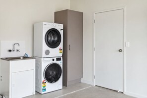 Een wasruimte met een gestapelde wasmachine en droger, een spoelbak met kraan, en een gesloten deur.