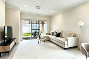 A modern living room with a flat-screen TV, a beige sofa, a coffee table, and a floor lamp. - 3BR Spring Mountain Home |Near Springfield Central (Spring Mountain)