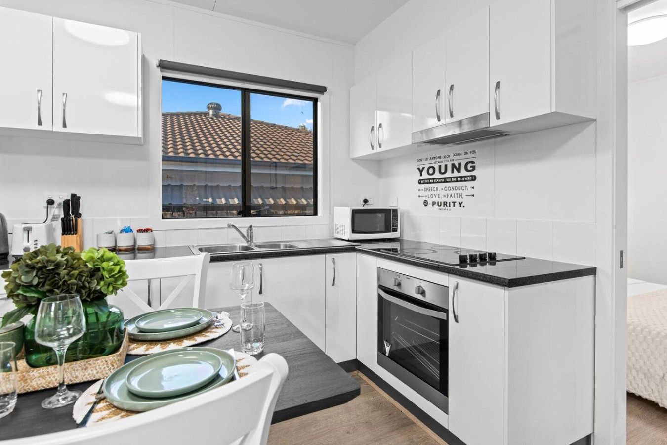 A modern kitchen with white cabinetry, a built-in microwave, and a dining area with a table set for two.