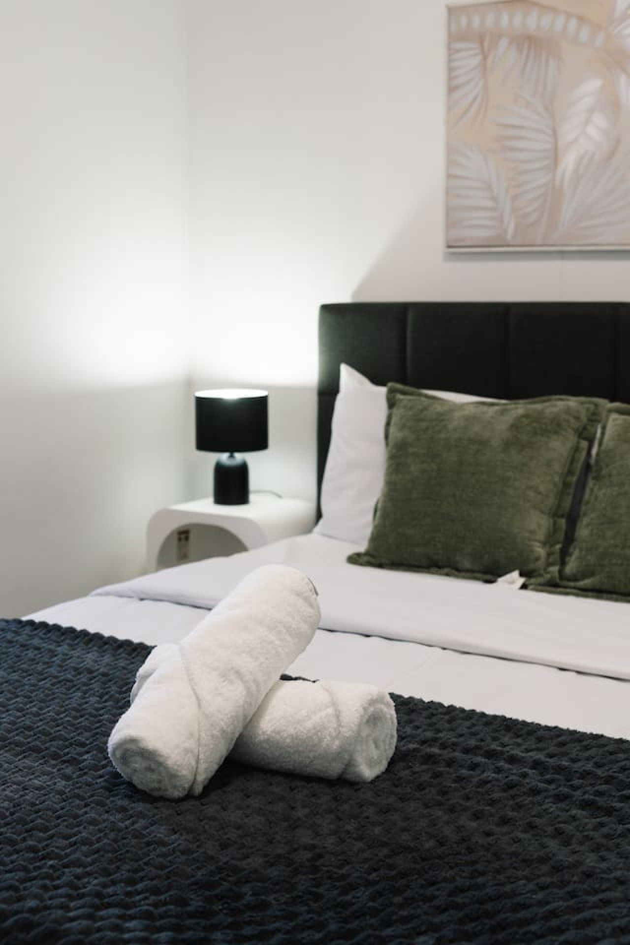 A neatly made bed with white linens, a dark gray blanket, and two pillows, one green and one white.