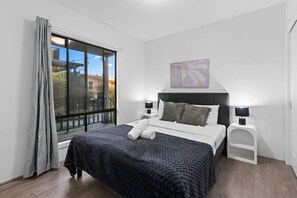 Ein modernes Schlafzimmer mit einem großen Bett, einem Fenster mit Vorhängen, einem Nachttisch und einer Wandlampe.