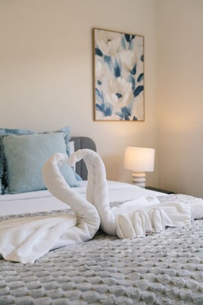 Een bed met een handdoekarrangement in de vorm van een zwaan, een blauw kussen en een abstract schilderij aan de muur.