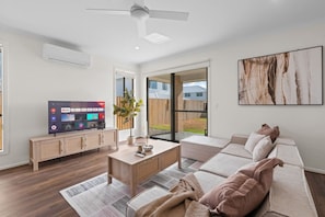 Ein modernes Wohnzimmer mit Fernseher, Couch, Holztisch und großem Fenster.