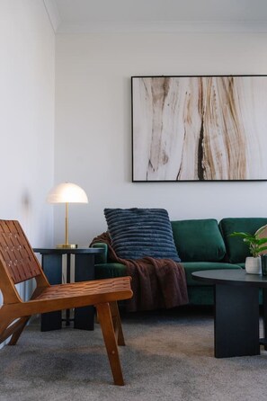 Ein modernes Wohnzimmer mit einem grünen Sofa, einem Holzstuhl, einer Lampe und einem großen abstrakten Gemälde an der Wand.