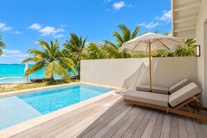 Un área de piscina con muelle de madera, sillones de descanso y vista al océano.